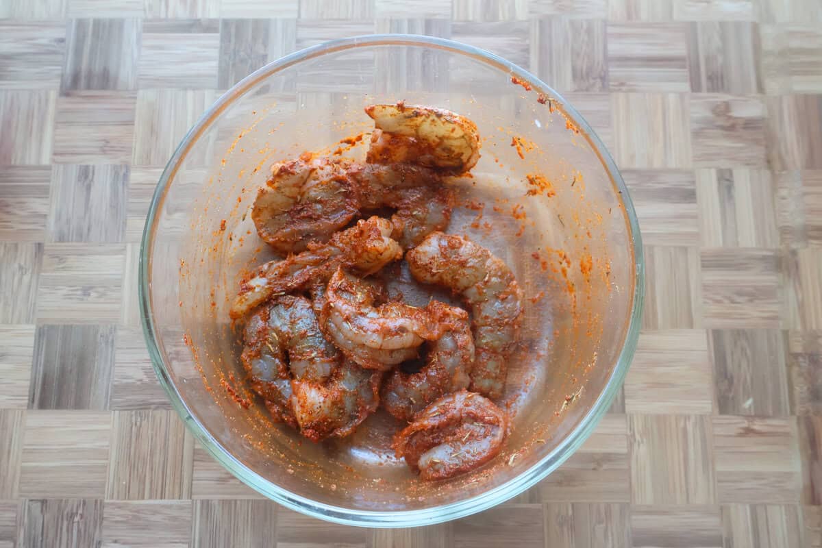 Shrimp marinating in a Cajun seasoning in a glass bowl on the counter.