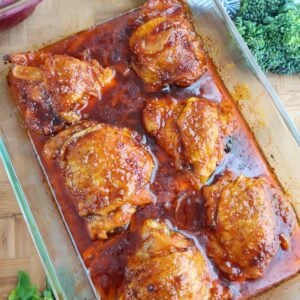 Baked BBQ chicken thighs glazed in barbecue sauce in a square glass baking dish