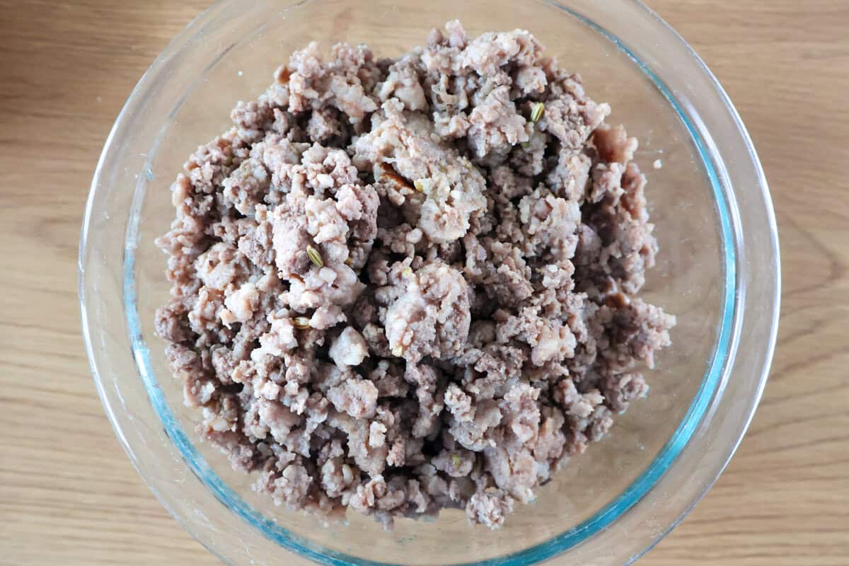 Cooked ground beef and Italian sausage in a glass bowl.