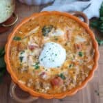 Lasagna soup topped with ricotta in an orange bowl.