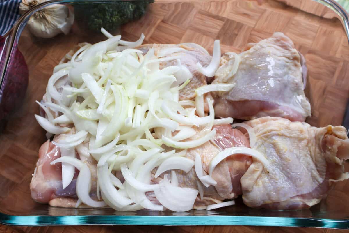 Raw chicken thighs topped with sliced white onion in a glass baking dish