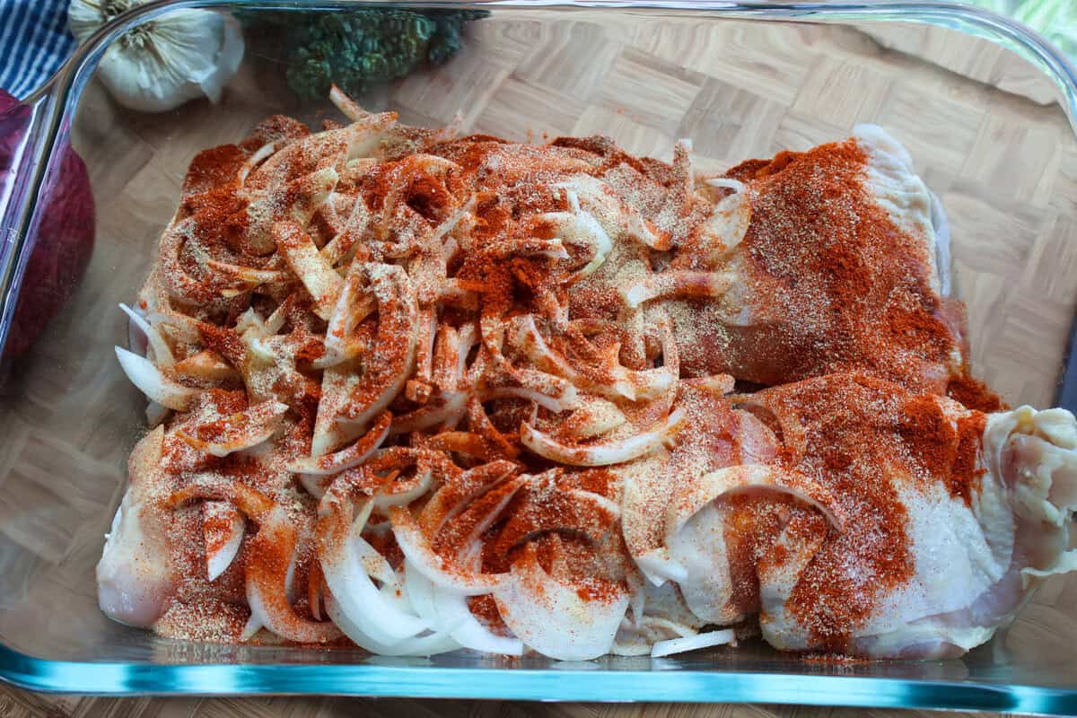 Raw chicken thighs and onion seasoned with paprika, garlic powder, and spices