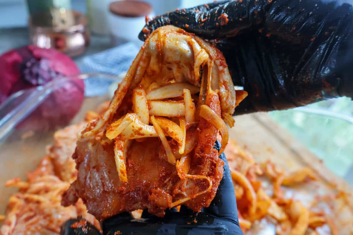 Stuffing onion slices under the skin of a seasoned chicken thigh