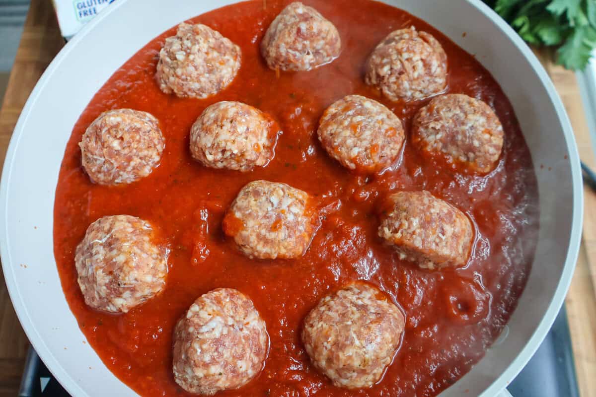 Meatballs simmering in marinara sauce in a skillet