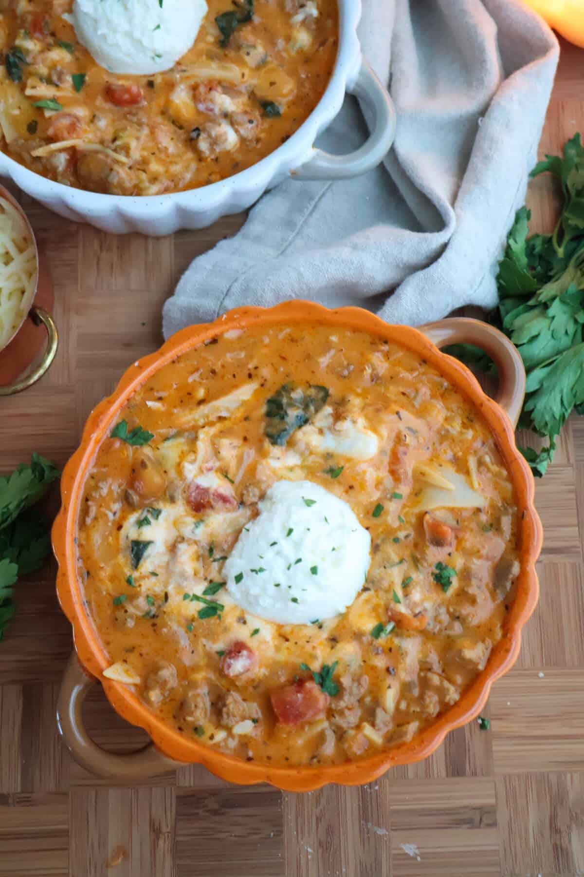 Lasagna soup topped with ricotta in an orange bowl, with a second bowl in the background.