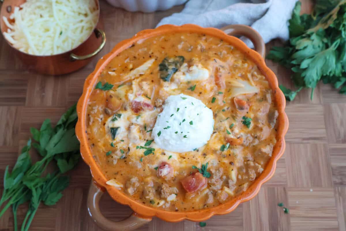 Close up of lasagna soup with ricotta and parsley in an orange bowl.