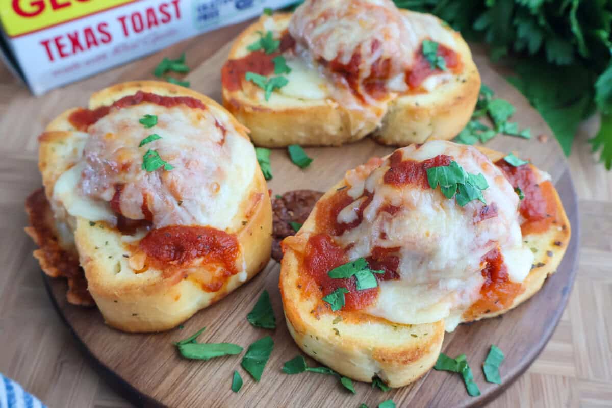 Close-up of baked Texas Toast Meatball Melts topped with melted cheese and fresh herbs