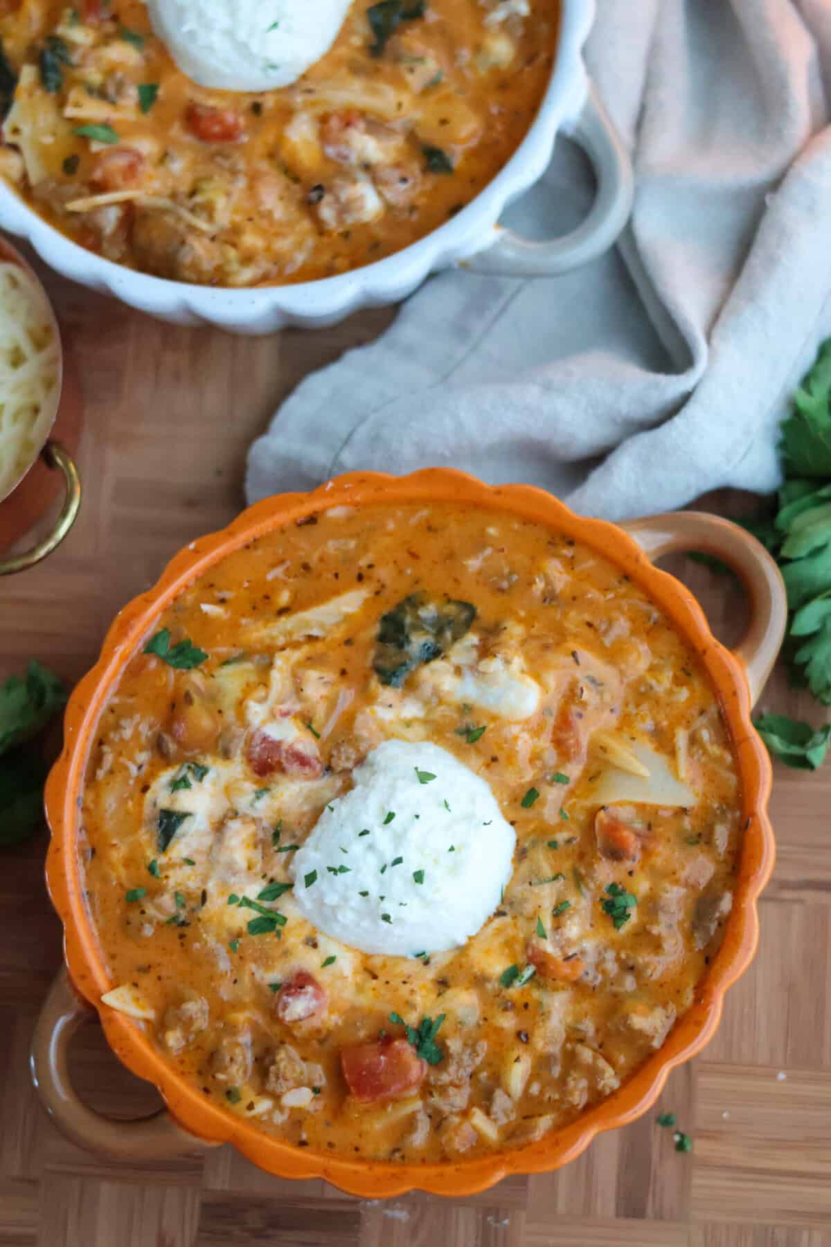 Two bowls of lasagna soup topped with ricotta and fresh parsley.