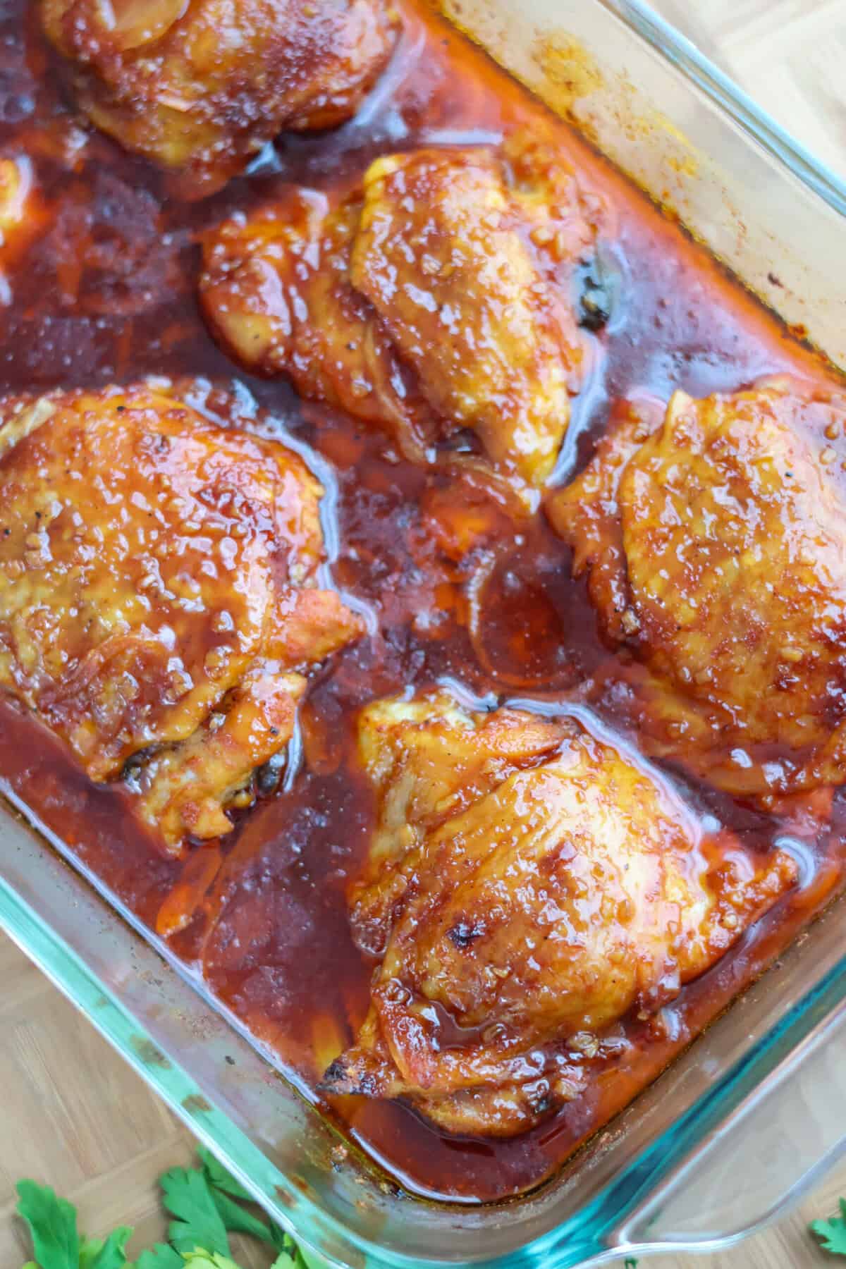 Close-up of baked BBQ chicken thighs coated in a sticky homemade barbecue glaze in a baking tray