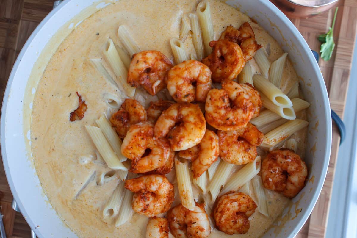 Penne and blackened shrimp being stirred into creamy Parmesan sauce for surf and turf pasta
