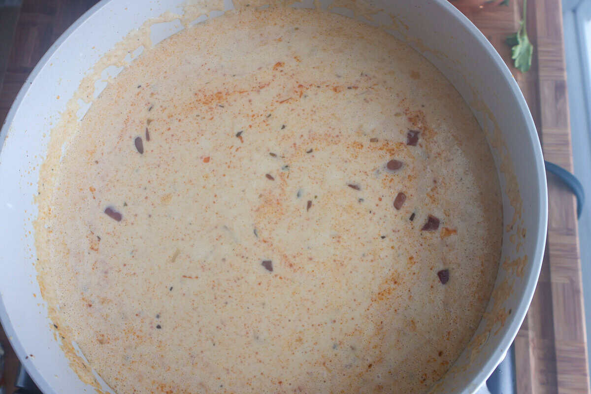 Heavy cream and chicken broth simmering into a creamy sauce in a skillet for surf and turf pasta
