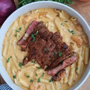 Creamy surf and turf pasta with sliced blackened ribeye steak and shrimp in a skillet