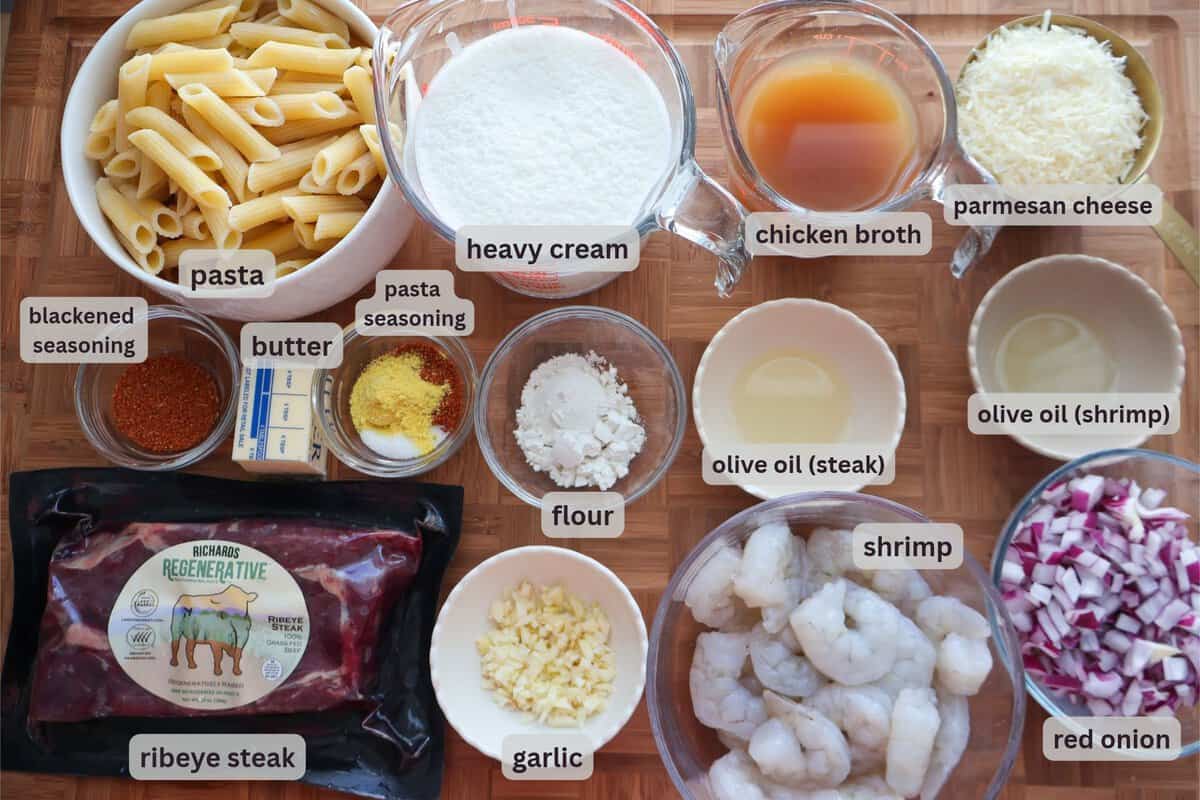 Ingredients for creamy surf and turf pasta: ribeye steak, shrimp, penne, heavy cream, chicken broth, Parmesan, butter, garlic, red onion and seasonings