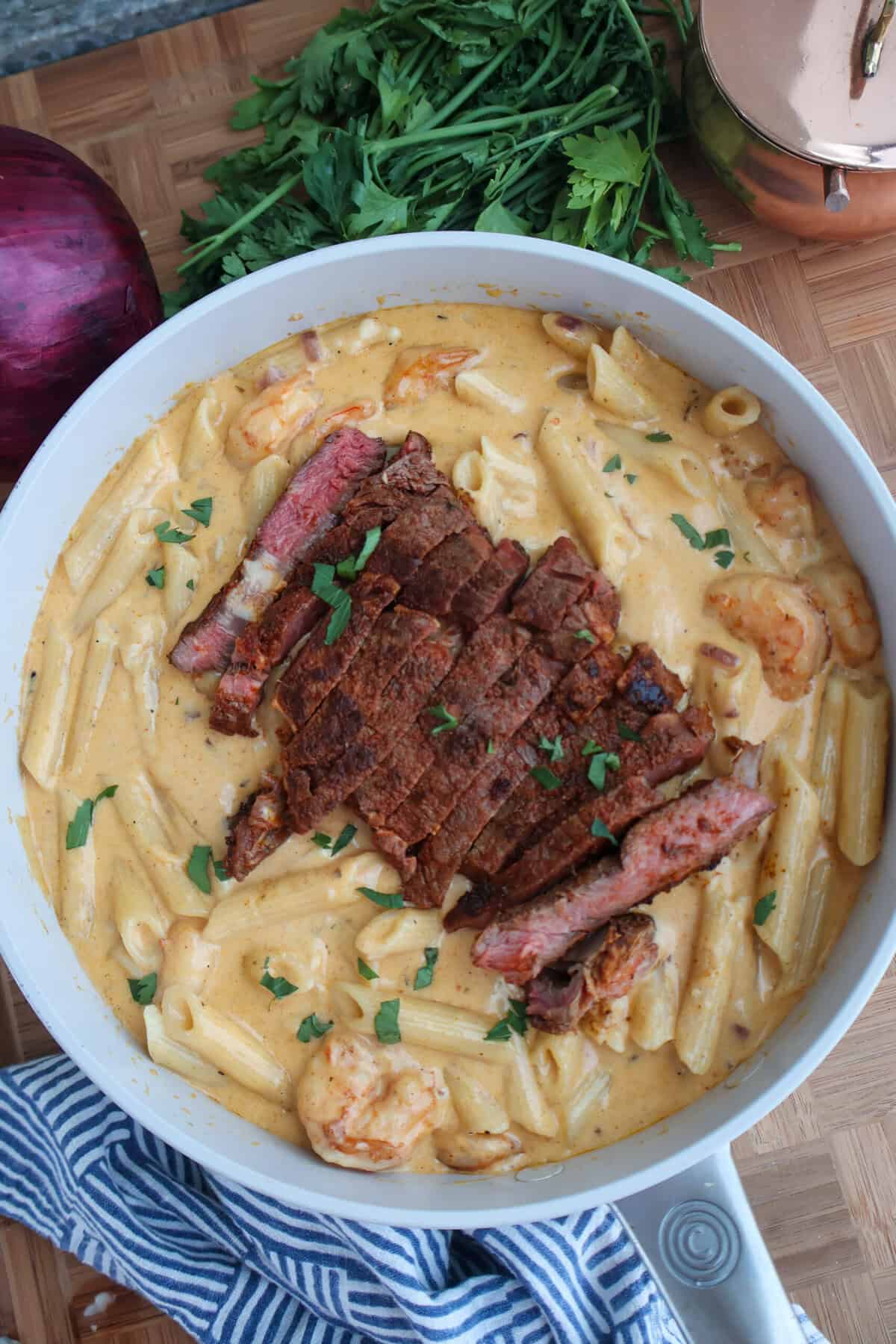 Creamy surf and turf pasta with sliced blackened ribeye steak and shrimp in a skillet