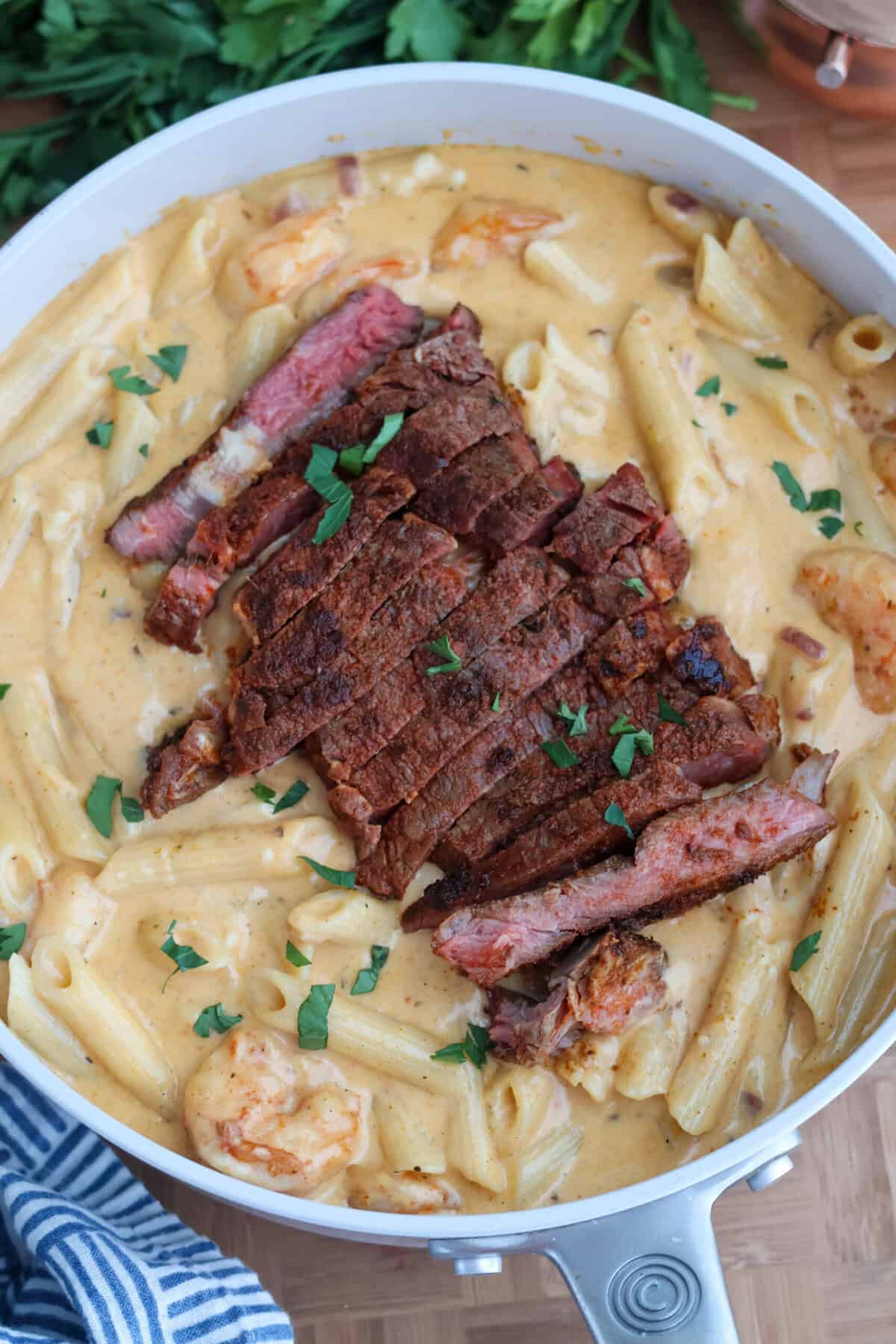 Creamy surf and turf pasta with sliced blackened ribeye, shrimp and Parmesan in a skillet