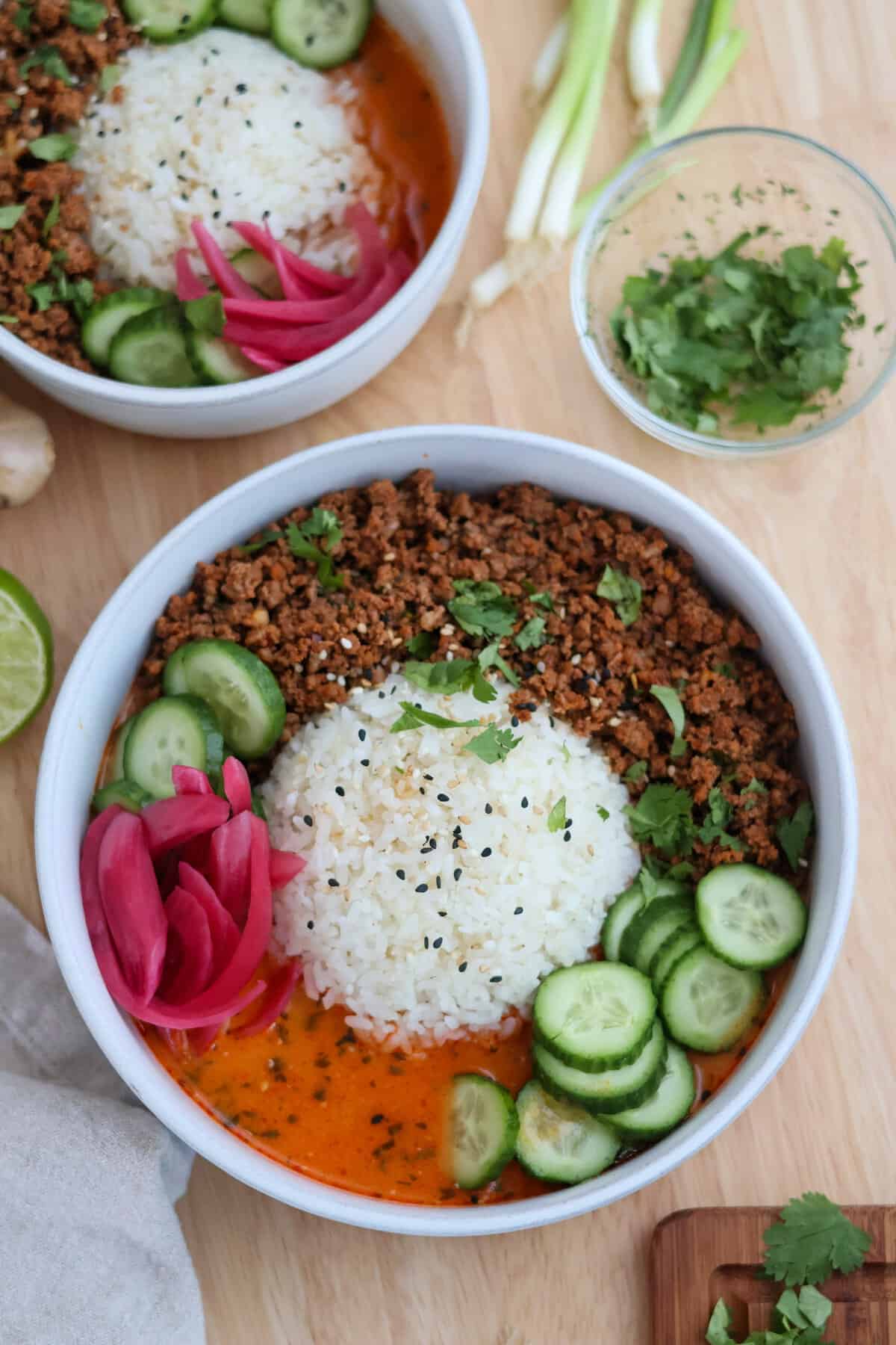 Two crispy beef broth bowls with crispy ground beef, rice, and creamy red curry broth, served with fresh cilantro and green onions