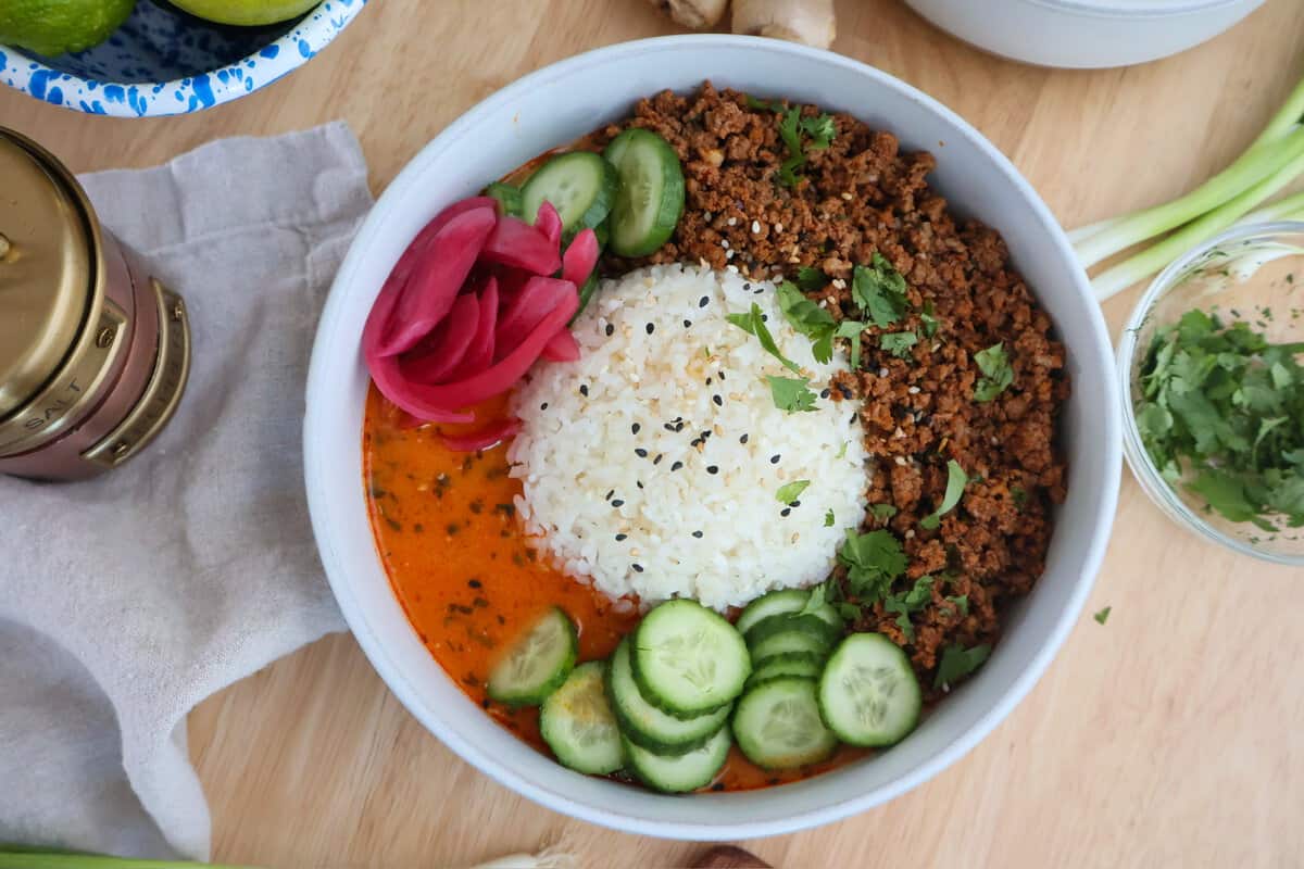Close-up of a crispy beef broth bowl with seasoned ground beef, rice, red curry coconut broth, and fresh toppings