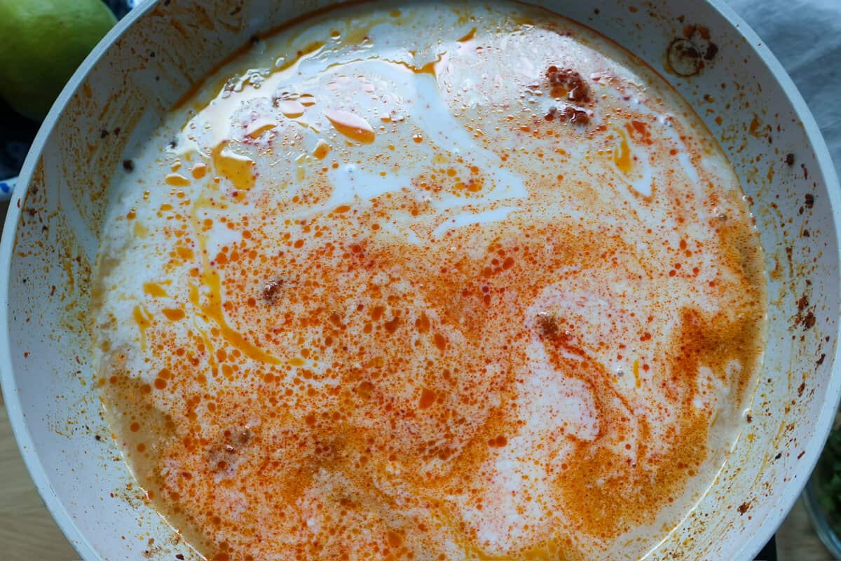 Red curry paste stirred into coconut milk and beef bone broth in a skillet