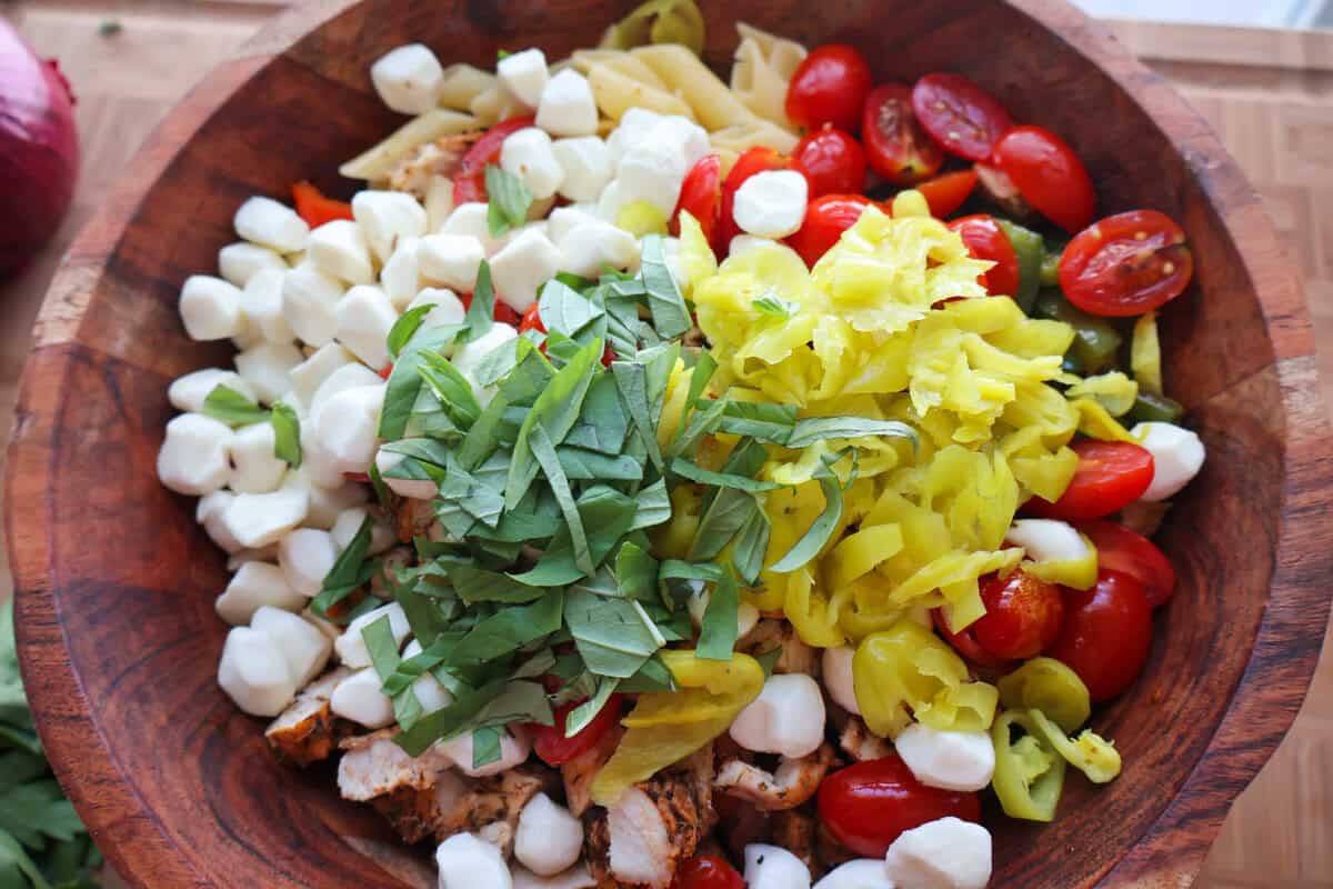 Pasta salad ingredients arranged in a large bowl before mixing.