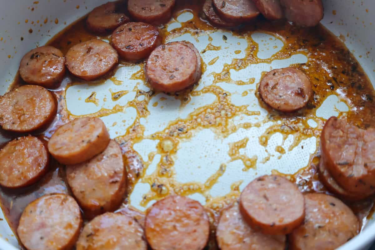 Sliced kielbasa browning in a skillet.