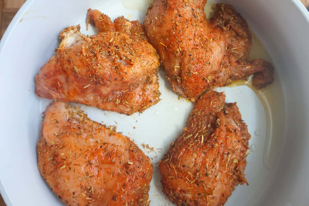 Seasoned raw chicken breasts searing in olive oil in a skillet.