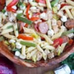 Gluten-free pasta salad with Italian dressing in a wooden bowl with chicken, kielbasa, peppers, and mozzarella pearls.