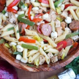 Gluten-free pasta salad with Italian dressing in a wooden bowl with chicken, kielbasa, peppers, and mozzarella pearls.