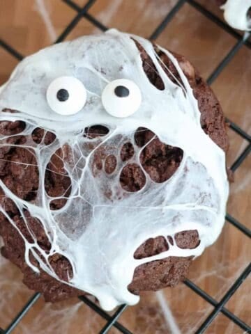Spider web cookie with marshmallow webs and candy googly eyes on a wire cooling rack