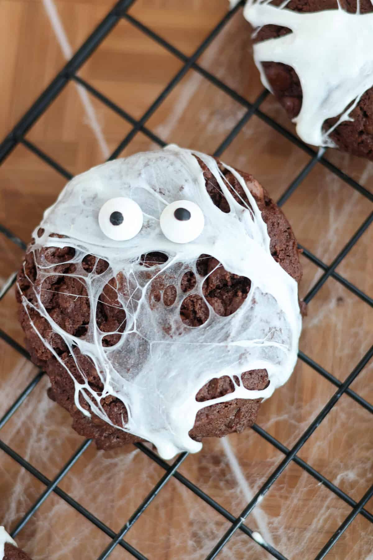 Spider web cookie with marshmallow webs and candy googly eyes on a wire cooling rack