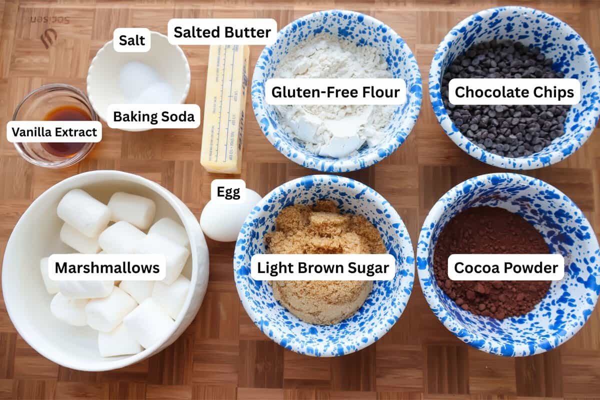 Ingredients for spider web cookies, including gluten-free flour, cocoa powder, chocolate chips, and marshmallows