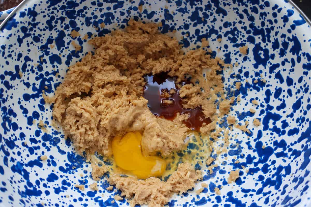 Egg and vanilla added to creamed butter and brown sugar in a speckled mixing bowl
